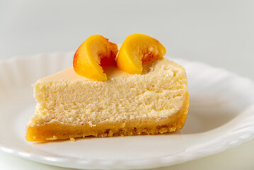 Cheesecake with slices of peach on plate on white background.