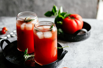 Tomato juice with ice in a glass on a gray background