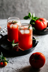 Tomato juice with ice in a glass on a gray background