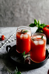 Tomato juice with ice in a glass on a gray background