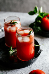 Tomato juice with ice in a glass on a gray background