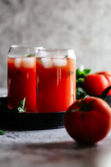 Fototapeta na wymiar Tomato juice with ice in a glass on a gray background