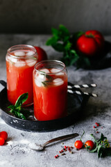 Tomato juice with ice in a glass on a gray background