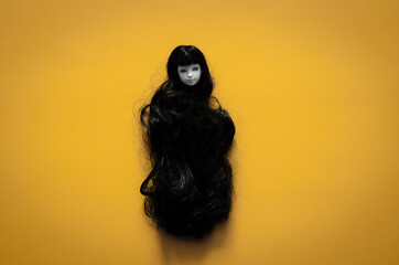 Long hair smiling female ghost doll on yellow background. Minimal Halloween scary concept.