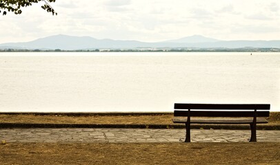 An empty wooden bench in a park facing Lake Trasimeno (Umbria, Italy, Europe)