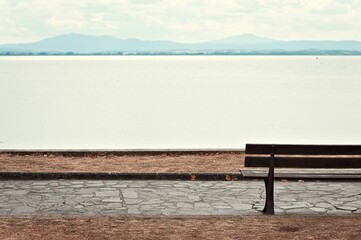 Fototapeta na wymiar An empty wooden bench in a park facing Lake Trasimeno (Umbria, Italy, Europe)