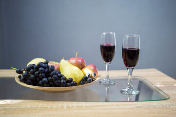 glasses with red wine on the table and a bowl with fruit grapes apple and pear