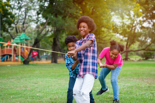 Group of African American boy and girl playing tug of war together in the park. Cheerful children with curly hair having fun with tug of war. Black children people playing tug of war