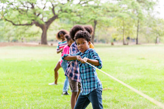 Group of African American boy and girl playing tug of war together in the park. Cheerful children with curly hair having fun with tug of war. Black children people playing tug of war