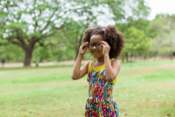 African American little girl with curly hair wearing glasses and playing in the park