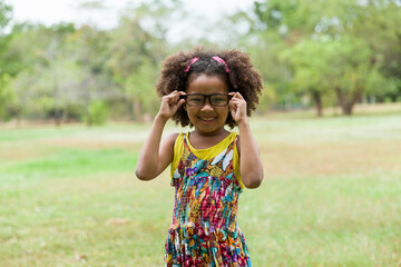 African American little girl with curly hair wearing glasses and playing in the park