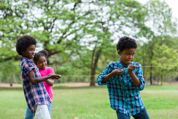Group of African American boy and girl playing tug of war together in the park. Cheerful children...