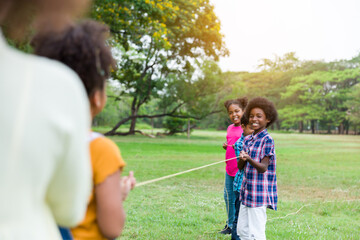 Group of African American boy and girl playing tug of war together in the park. Cheerful children...