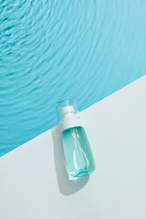 Blue cosmetic bottle on white podium and the blue water surface. Blank label for branding mock-up....