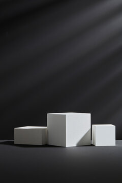 Empty White podium on dark background with light strecks. Black geometric background can be used for commercial advertising, cosmetics and beauty product. 