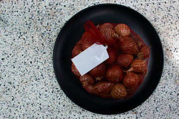 Shallots in mesh bags with white labels on black plates.