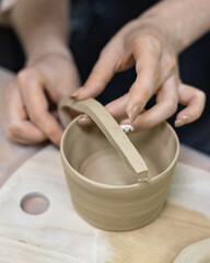the potter's hands sculpt a handle on the blank of a clay mug