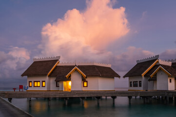 Over water bungalows with steps into amazing green lagoon at sunset time. Crossroads Maldives, july...