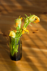 Autumn still life: zucchini flowers intransparent glass on wooden table 