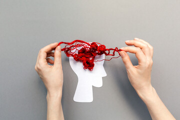 Female's hands unravel the tangled red threads on the silhouette of the head, representing the...