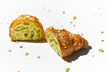Sweet croissant with pistachio paste and nuts on a white plate. Hard light