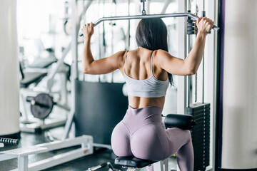 Fitness young woman working out in gym doing exercise for back. Athletic girl doing lat pulldown