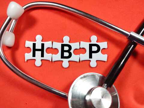 Text HBP (High Blood Pressure) writing on jigsaw puzzle with stethoscope on red background.
