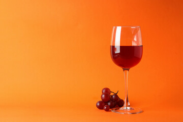 Glasses of red wine and grape on orange background
