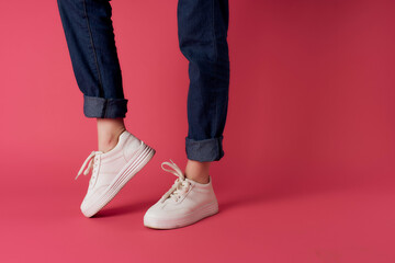 inverted female legs in white sneakers pink background cropped view studio