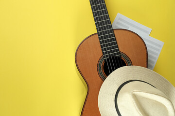 Classical guitar, music sheets and hat on yellow background