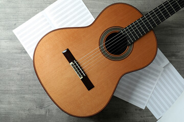 Classical guitar and music sheets on gray textured table