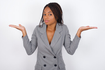 Puzzled and clueless Young african american business woman with braids over white wall with arms out, shrugging shoulders, saying: who cares, so what, I don't know. - obrazy, fototapety, plakaty