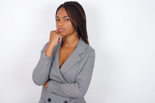 Portrait of thoughtful Young african american business woman with braids over white  keeps hand under chin, looks away trying to remember something or listens something with interest. Youth concept.