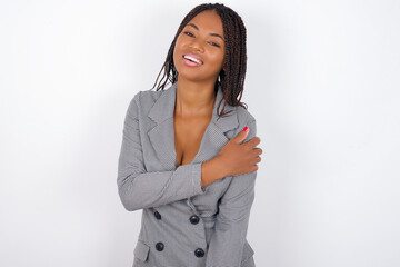 People, lifestyle, youth and happiness concept. Shy pretty Young african american business woman with braids over white wall, feeling happy hugging herself.