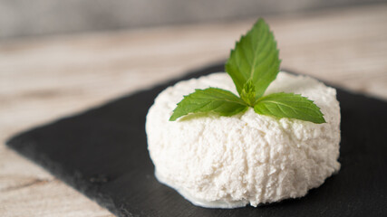 Fresh cottage cheese with mint on a black plate. Ricotta cheese isolated. House cottage cheese nutrition