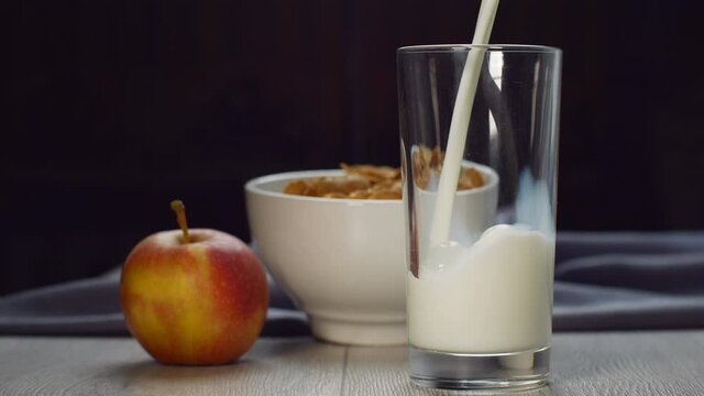 pouring milk into a glass glass on a wooden table. Healthy breakfast in the morning. Cereals, fruits and milk
