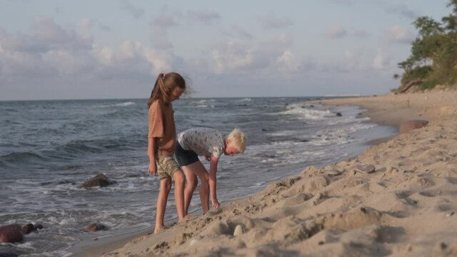 A boy and a girl walk along the beach by the sea in the summer. A schoolboy boy paints on the sand on the beach.