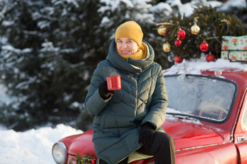Fototapeta na wymiar Senior woman in warm winter clothes standing in the street with cups of tea. merry Christmas!