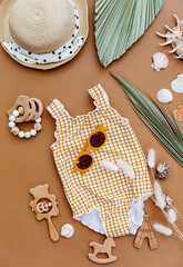 Set of summer baby swimsuit and accessories on brown background. Holiday child outfit. Flat lay, top view