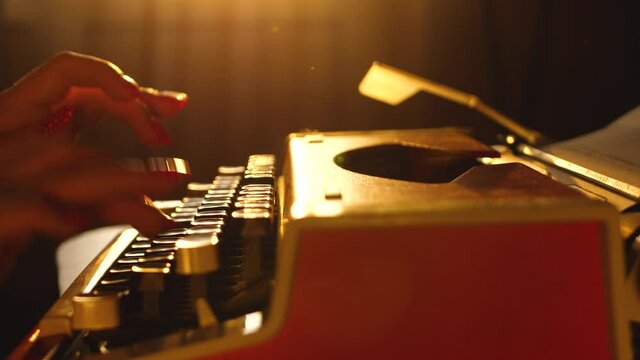 Female hand type text on stationary mechanical typewriter. English language. Paperwork and typescript. Woman typist secretary work on letter or correspondence. Dramatic warm color silhouette on sunset