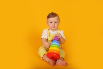 A beautiful blue-eyed little boy in a yellow suit is playing a multi-colored toy pyramid