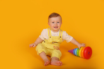 A beautiful blue-eyed little boy in a yellow suit is playing a multi-colored toy pyramid