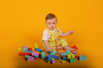 a beautiful blue-eyed little boy in a yellow suit plays with colorful toys