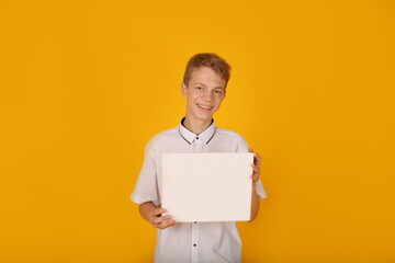 a handsome guy in a white shirt holds a white sheet of paper yellow background