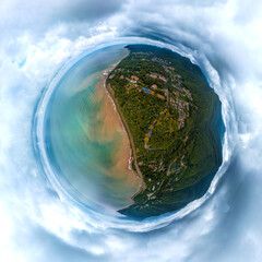 aerial drone landscape of the sea coast near forested mountains on a rainy summer day. The water in the sea is muddy and dirty due to rain streams flowing down from the mountains. Little planet view