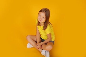 Obraz premium a beautiful brown-haired girl in a yellow T-shirt and shorts is sitting on a yellow background