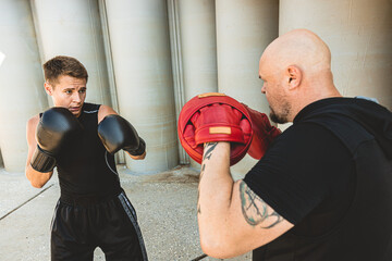 Two men exercising and fighting in outside. Boxer in gloves is training with a coach