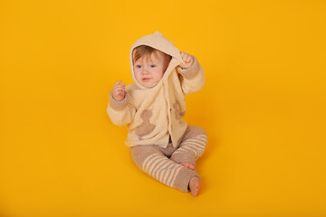 a beautiful blue-eyed baby is sitting on a yellow background in a knitted suit