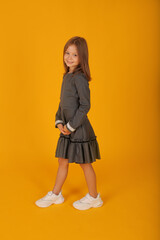 beautiful brown-haired girl in a gray school dress yellow background