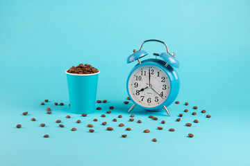 Blue Сup of coffee beans and alarm clock on a blue background with scattered coffee beans